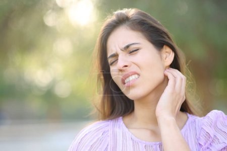 Téléchargez les photos : Femme stressée griffant le cou après une piqûre d'insecte dans un parc - en image libre de droit