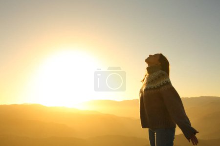 Téléchargez les photos : Portrait latéral d'une femme détendue respirant l'air frais au coucher du soleil dans la montagne en hiver - en image libre de droit