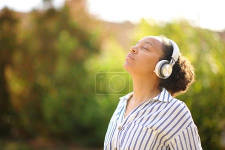 Photo for Black woman meditating using headphone in a park - Royalty Free Image