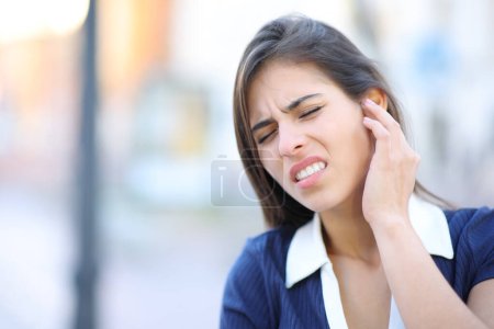 Téléchargez les photos : Femme stressée se plaignant mal aux oreilles dans la rue - en image libre de droit