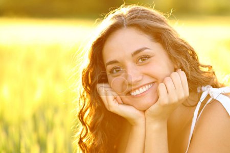 Téléchargez les photos : Femme heureuse souriant avec des dents parfaites posant dans un champ au coucher du soleil - en image libre de droit