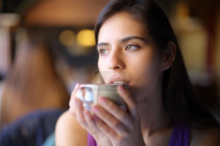 Photo for Pensive woman drinking coffee looking away in a restaurant - Royalty Free Image