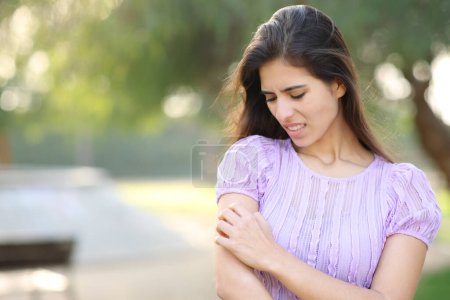 Mujer rascándose el brazo de pie en un parque en temporada de verano