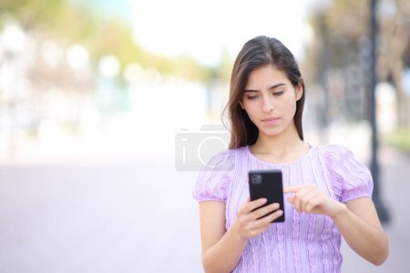 Téléchargez les photos : Avant vire d'une femme marchant en utilisant un téléphone portable dans la rue - en image libre de droit