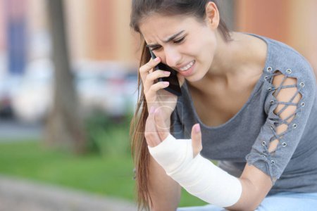 Photo for Convalescent woman with bandaged arm calling doctor on phone sitting in the street - Royalty Free Image
