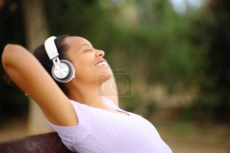 Photo for Profile of a black woman wearing headphone relaxing listening music in a park - Royalty Free Image