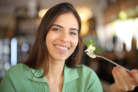 Foto de Mujer feliz sosteniendo tenedor con lechuga en un restaurante mirando a la cámara - Imagen libre de derechos