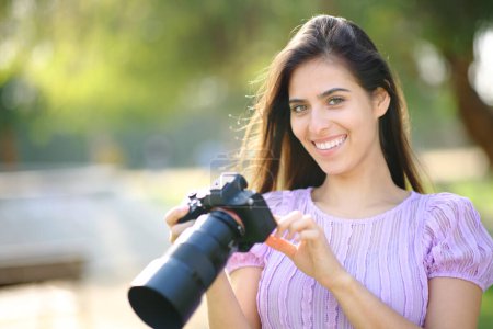 Téléchargez les photos : Joyeux photographe vérifiant appareil photo vous regardant dans un parc - en image libre de droit