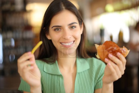 Foto de Feliz cliente del restaurante sosteniendo patata y sándwich mirándote - Imagen libre de derechos