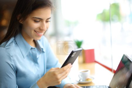 Téléchargez les photos : Femme heureuse utilisant un téléphone portable et une tablette dans un bar intérieur - en image libre de droit