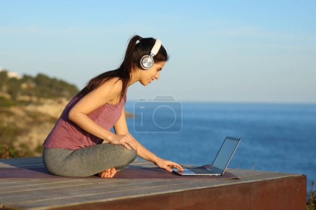 Photo for Yogi with headphone and laptop preparing online guided class on the beach - Royalty Free Image