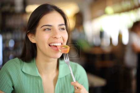 Foto de Mujer feliz comiendo tomate en un restaurante interior mirando hacia otro lado - Imagen libre de derechos