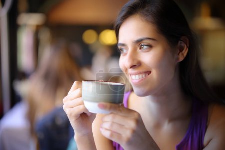 Foto de Mujer feliz sosteniendo taza de café mira al lado en un restaurante - Imagen libre de derechos