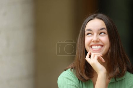 Téléchargez les photos : Vue de face d'une femme heureuse regardant côté se demandant dans la rue - en image libre de droit
