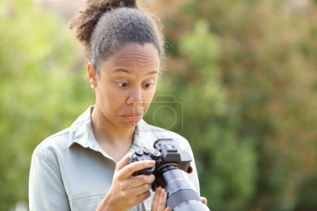 Foto de Perplejo fotógrafo negro revisando cámara sin espejo en un parque - Imagen libre de derechos