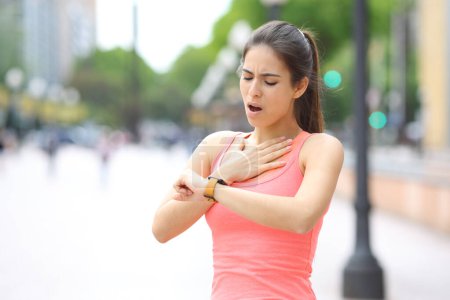 Runner choking and checking pulsations on smartwatch after soprt in the street