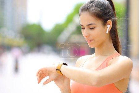 Foto de Corredor con auricular comprobando smartwatch en la calle - Imagen libre de derechos
