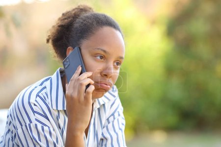 Foto de Mujer negra impaciente quejándose de hablar por teléfono en un parque - Imagen libre de derechos