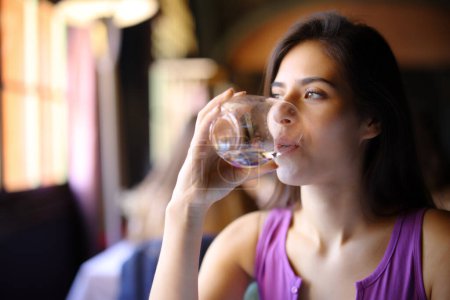 Téléchargez les photos : Femme eau potable à partir de verre assis dans un restaurant intérieur - en image libre de droit