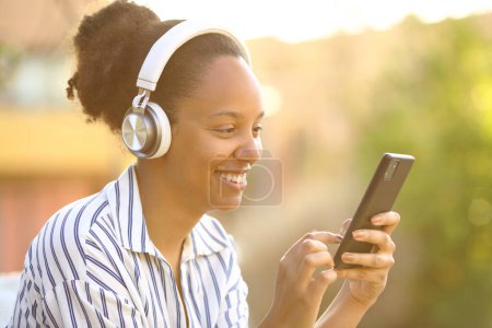 Téléchargez les photos : Femme noire écoutant de la musique au téléphone dans un parc au coucher du soleil - en image libre de droit