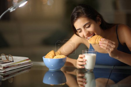 Photo for Happy woman eating pastries with milk alone in the night at home - Royalty Free Image