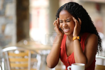 Photo for Black woman suffering migraine sitting in a coffee shop terrace - Royalty Free Image
