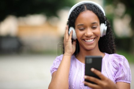 Téléchargez les photos : Portrait d'une femme noire heureuse écoutant de la musique dans la rue - en image libre de droit