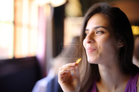 Photo for Happy restaurant customer eating chips looking away - Royalty Free Image