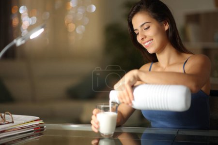 Téléchargez les photos : Femme heureuse remplissant le verre avec du lait dans la nuit à la maison - en image libre de droit