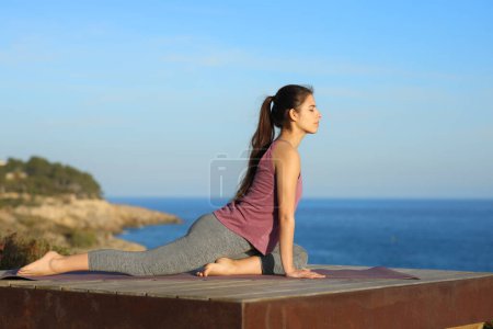 Foto de Retrato de una mujer haciendo yoga en una terraza de madera en la playa - Imagen libre de derechos
