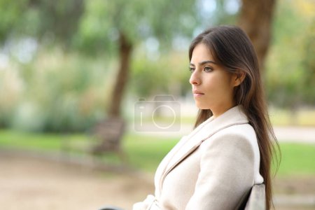 Photo for Serious woman in winter looks away on a bench in a park - Royalty Free Image