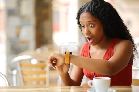 Photo for Amazed black woman checking smartwatch in a bar terrace - Royalty Free Image