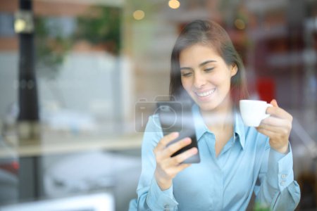 Téléchargez les photos : Femme heureuse buvant et utilisant un téléphone intelligent dans un bar intérieur - en image libre de droit