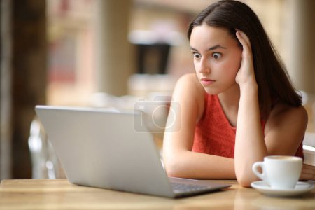 Téléchargez les photos : Femme choquée regardant le contenu de l'ordinateur portable dans une terrasse du bar - en image libre de droit