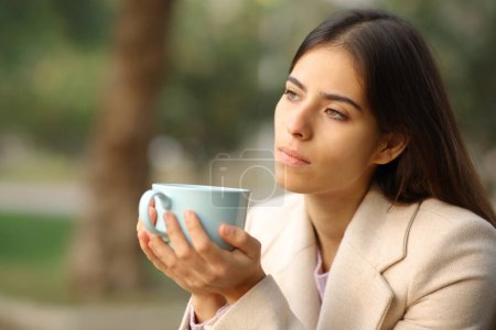 Téléchargez les photos : Femme pensive en hiver tenant une tasse de café dans un parc - en image libre de droit