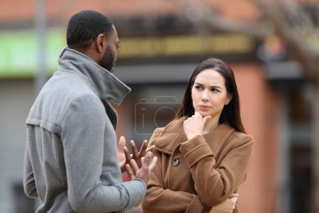 Téléchargez les photos : Femme suspecte écoutant un homme parler en hiver dans la rue - en image libre de droit
