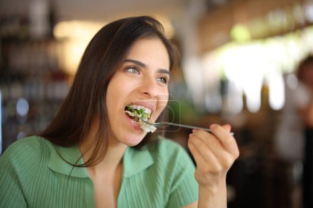 Foto de Mujer comiendo lechuga en un restaurante mirando hacia otro lado - Imagen libre de derechos