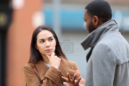 Photo for Doubtful woman listening a man talking in the street in winter - Royalty Free Image