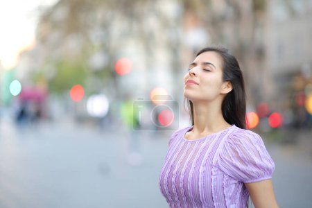 Téléchargez les photos : Femme satisfaite respirant de l'air frais dans une grande rue - en image libre de droit