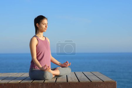 Photo for Yogi doing yoga in a wooden platform in the coast with the sea and horizon in the background - Royalty Free Image