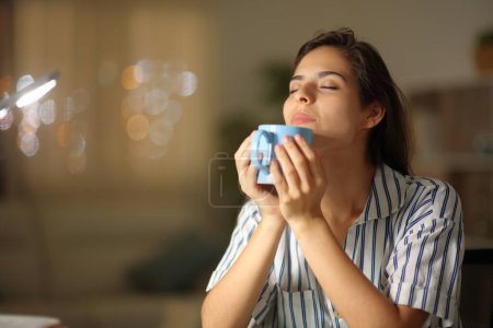 Foto de Mujer oliendo café caliente sentado en casa en la noche - Imagen libre de derechos