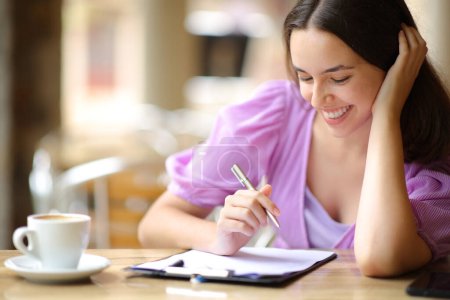 Téléchargez les photos : Heureuse femme lisant et remplissant le formulaire dans une terrasse restaurant - en image libre de droit