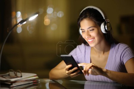 Foto de Mujer feliz con heaphone comprobando el teléfono por la noche en casa - Imagen libre de derechos