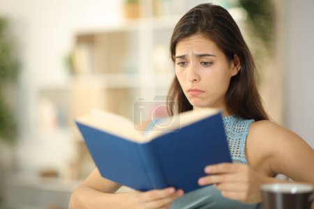 Photo for Sad woman reading a paper book sitting at home - Royalty Free Image