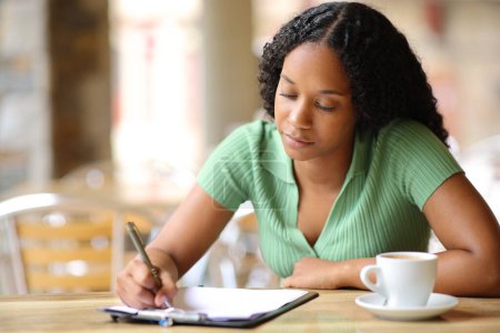 Téléchargez les photos : Femme noire remplissant un formulaire ou une enquête assis dans un bar terrasse - en image libre de droit