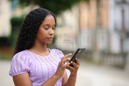 Téléchargez les photos : Femme noire utilisant un téléphone portable marchant dans la rue - en image libre de droit