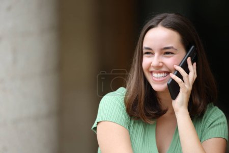 Photo for Happy female is talking on phone looking at side in the street - Royalty Free Image