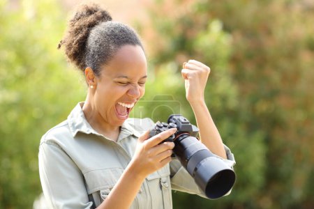 Photo for Excited black photographer checking good result standing in a park - Royalty Free Image
