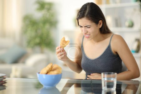 Foto de Glutton mujer que sufre dolor de estómago comer panadería en casa - Imagen libre de derechos