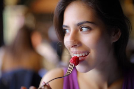 Photo for Happy woman eating blackberry looking at side sitting in a restaurant - Royalty Free Image